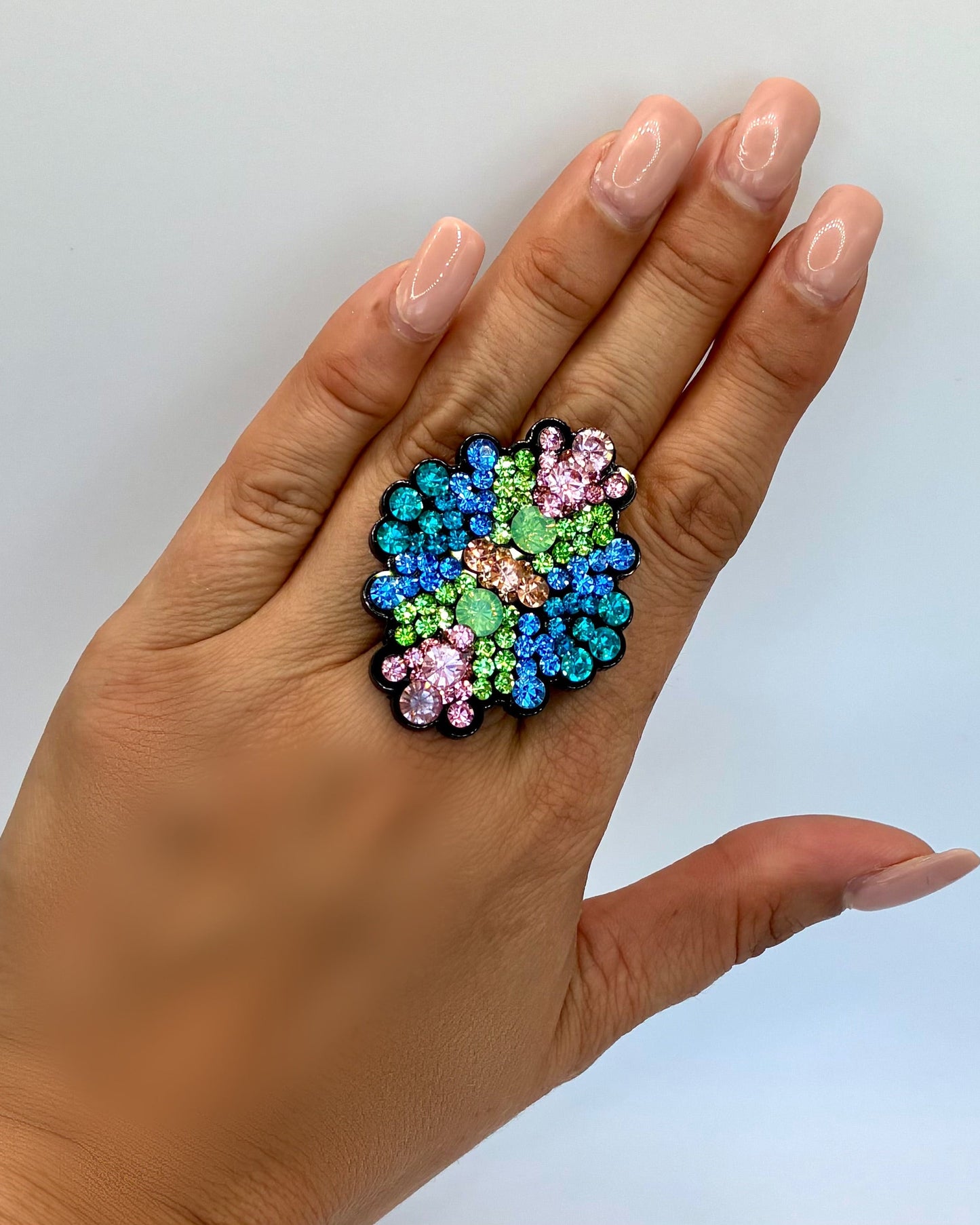 Hand wearing a colorful gemstone ring on a light background