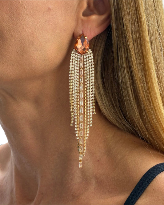 Close-up of a woman wearing a dangling earring with a large orange gemstone.