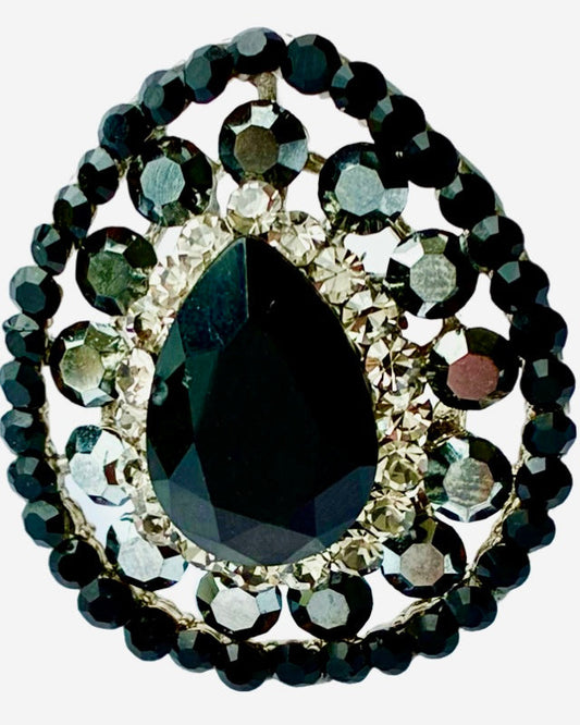 This image features an elegant piece of jewelry known as the "Black Eye drop." The centerpiece of the piece is a striking large black teardrop-shaped gemstone, which is surrounded by a beautifully arranged circle of smaller clear and dark gray crystals.