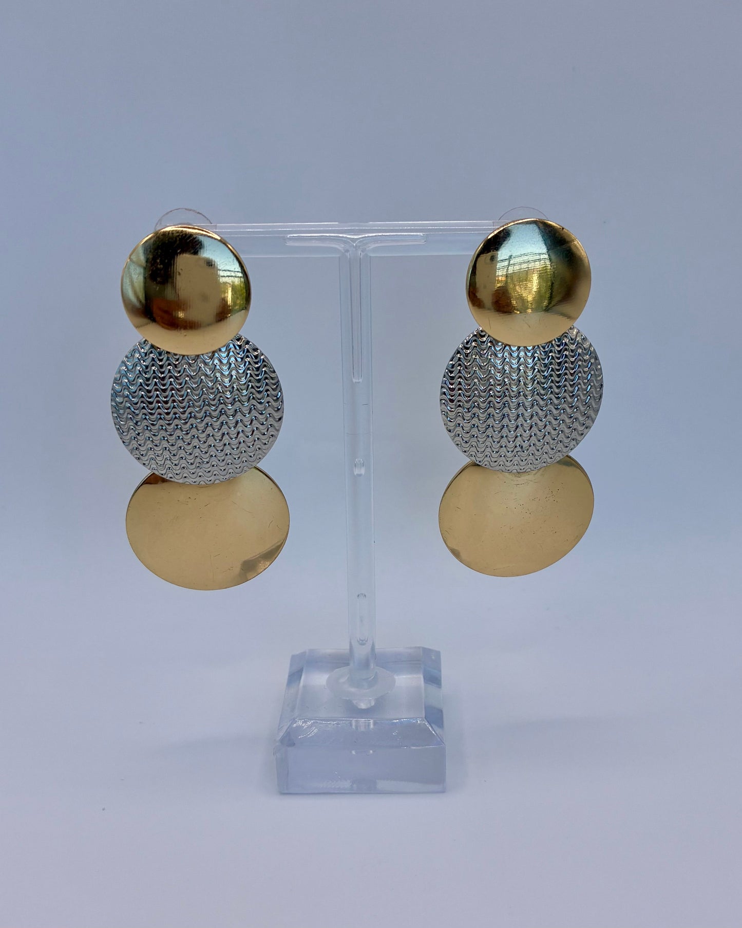 Gold and silver sphere earrings on a clear stand against a light gray background