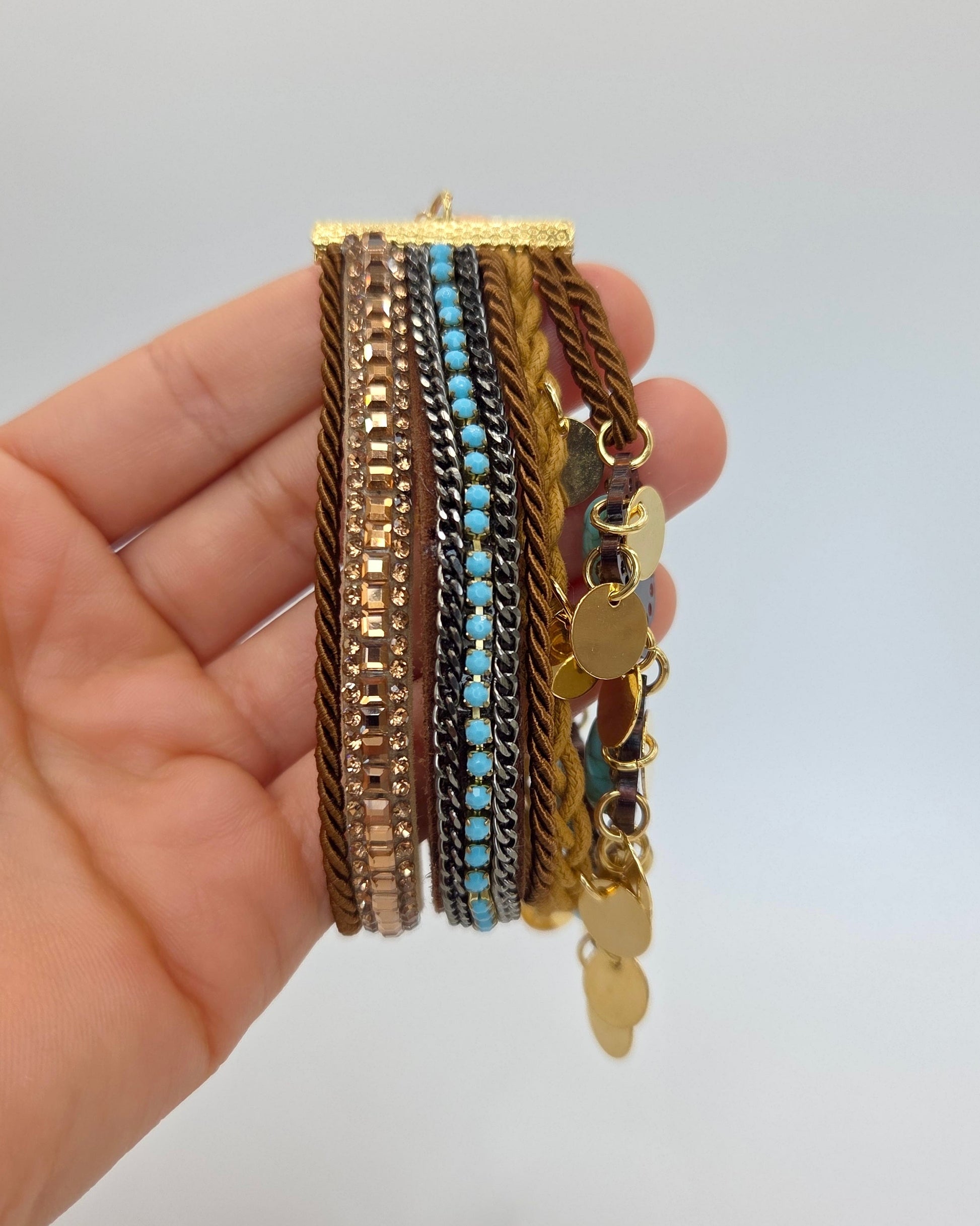 Hand holding a stack of gold and turquoise bracelets against a light gray background