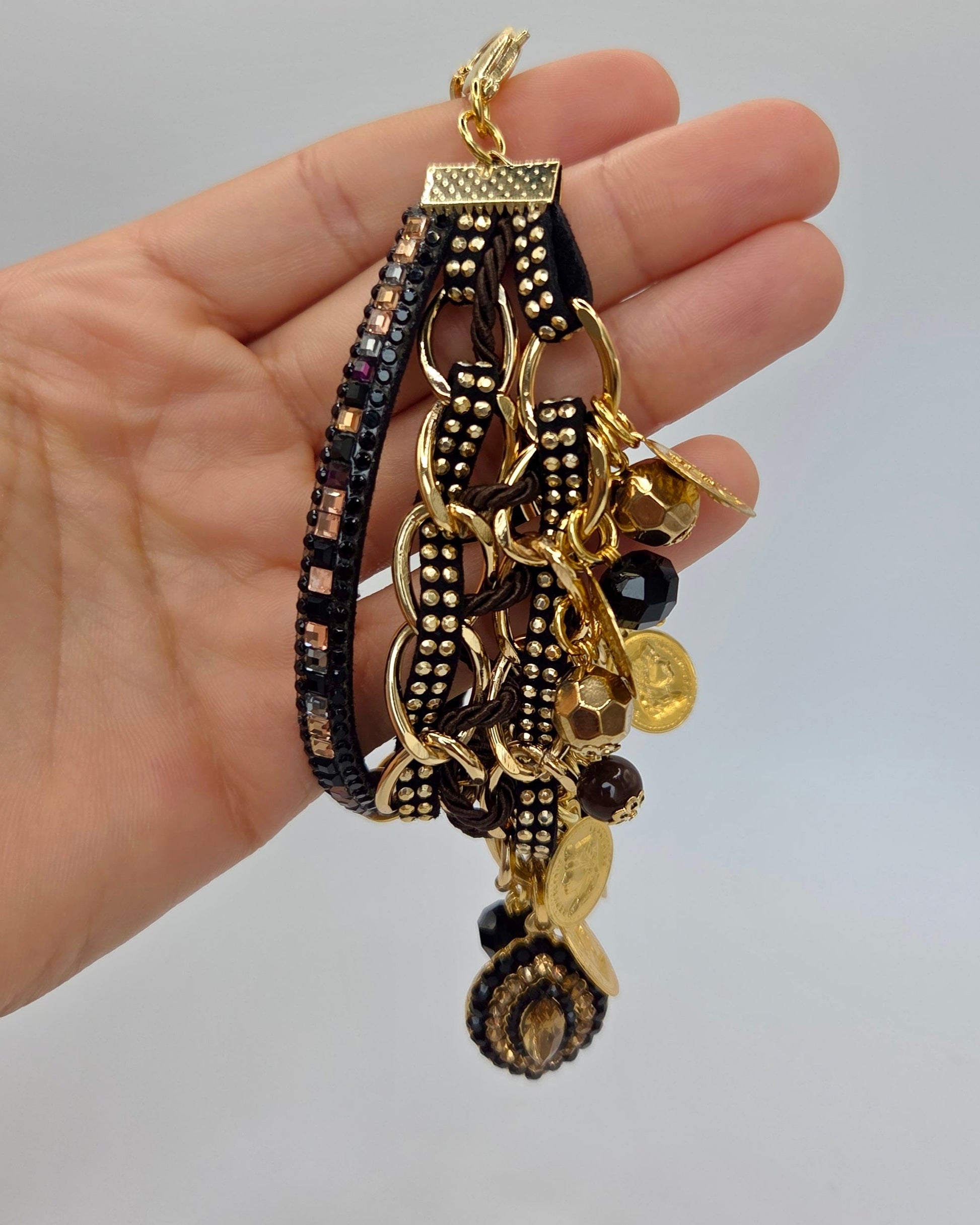 Hand holding a gold and black bracelet with charms against a gray background