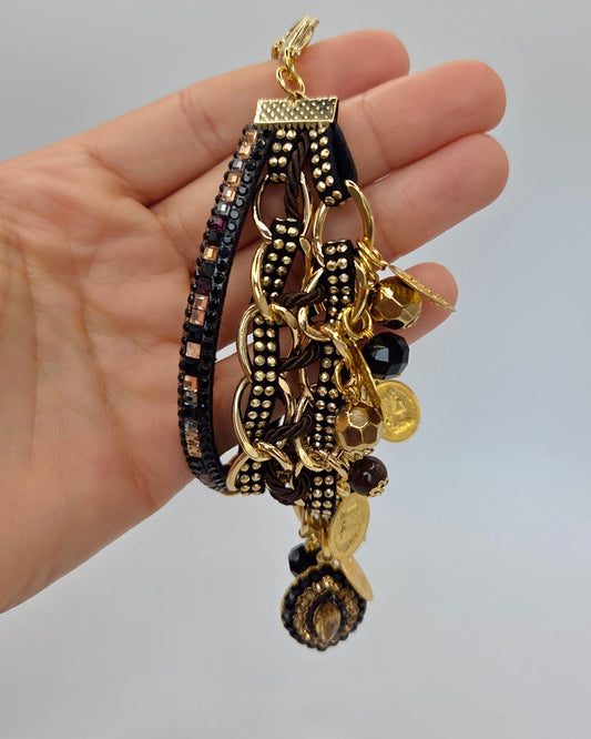 Hand holding a gold and black bracelet with charms against a gray background