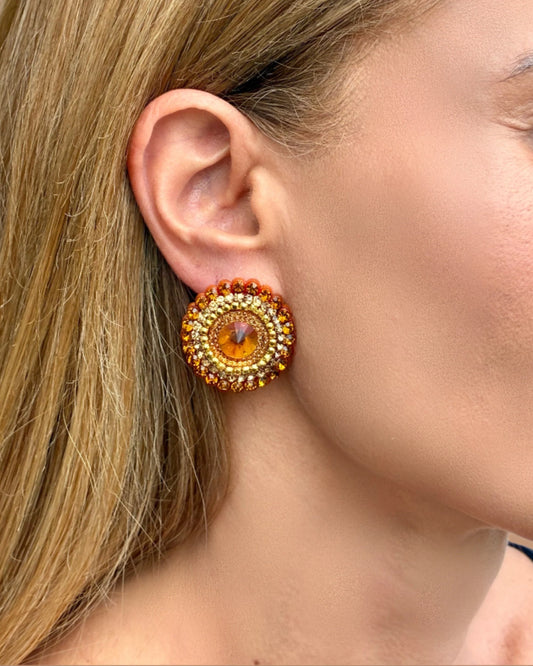 Close-up of a woman wearing a round, orange earring with gold accents.