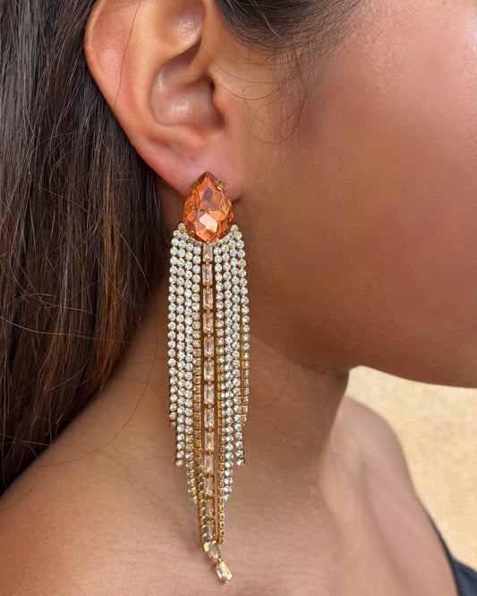 Close-up of an earring with a large orange gemstone and pearl tassels.
