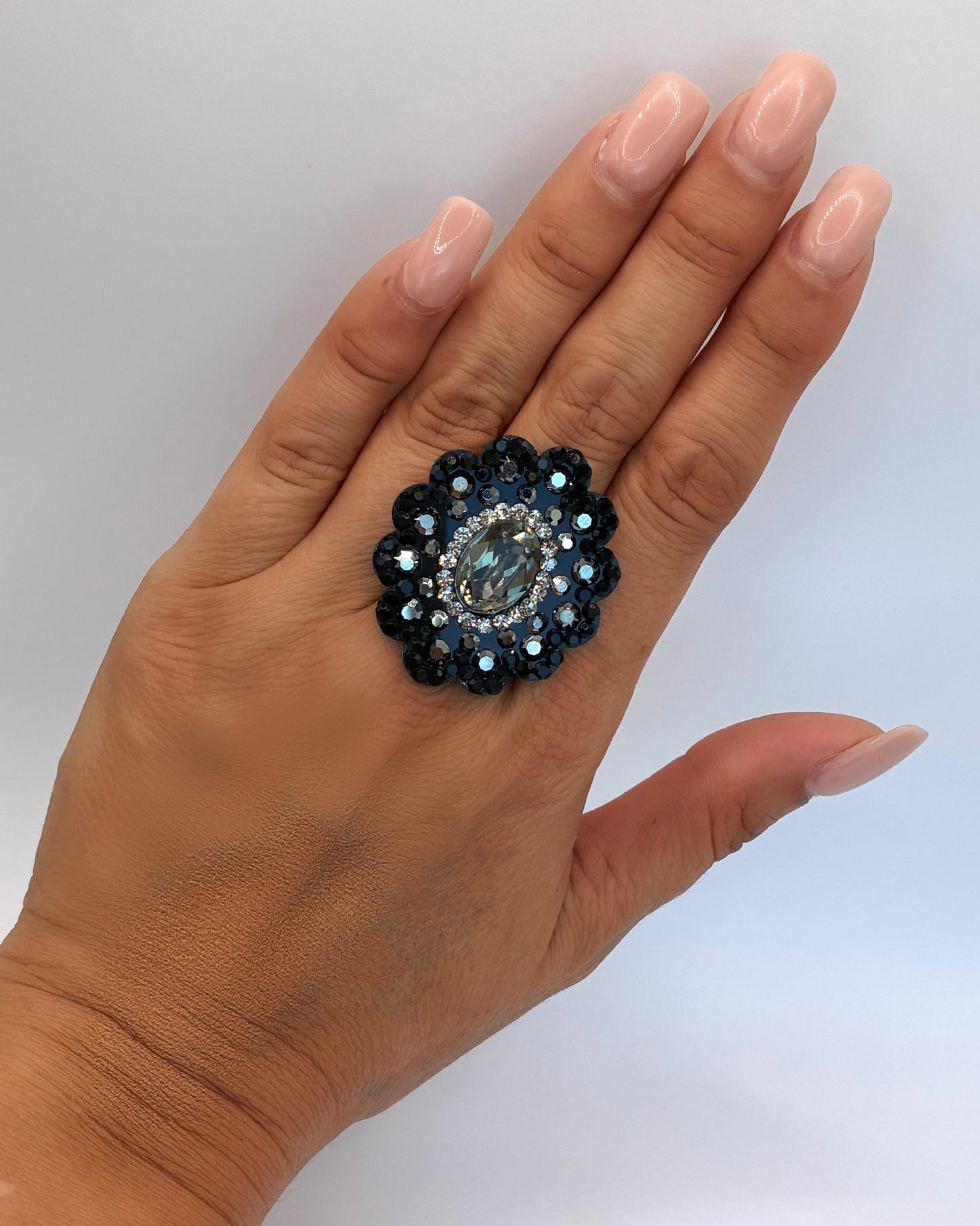 Hand wearing a decorative ring with a blue gemstone on a white background