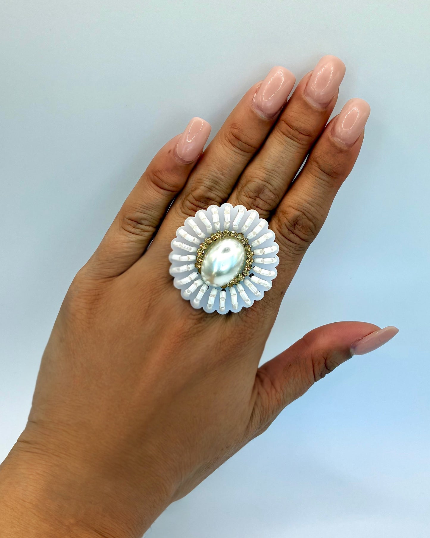Hand wearing a decorative ring with a white gemstone on a light blue background