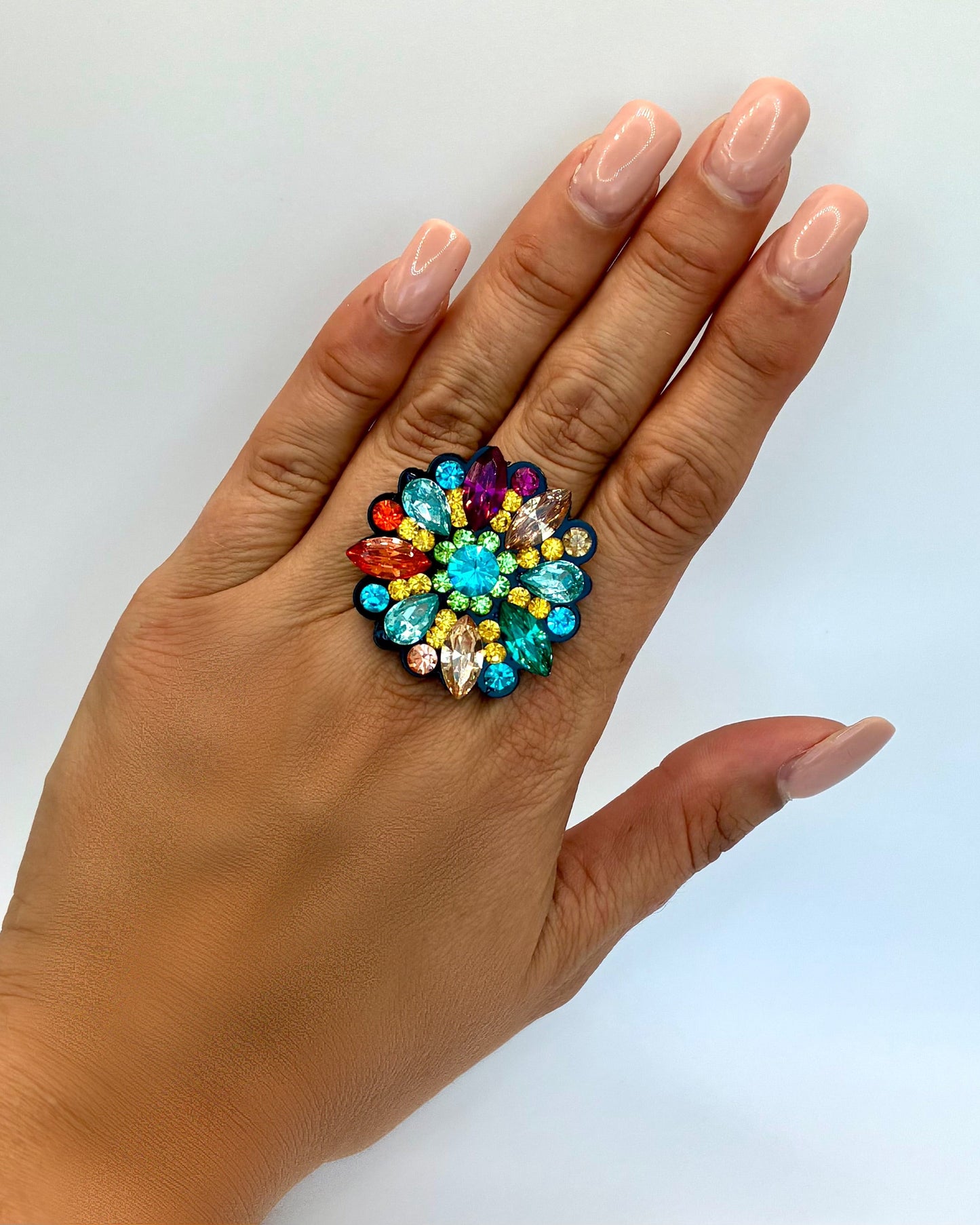 Hand wearing a colorful gemstone ring on a light background