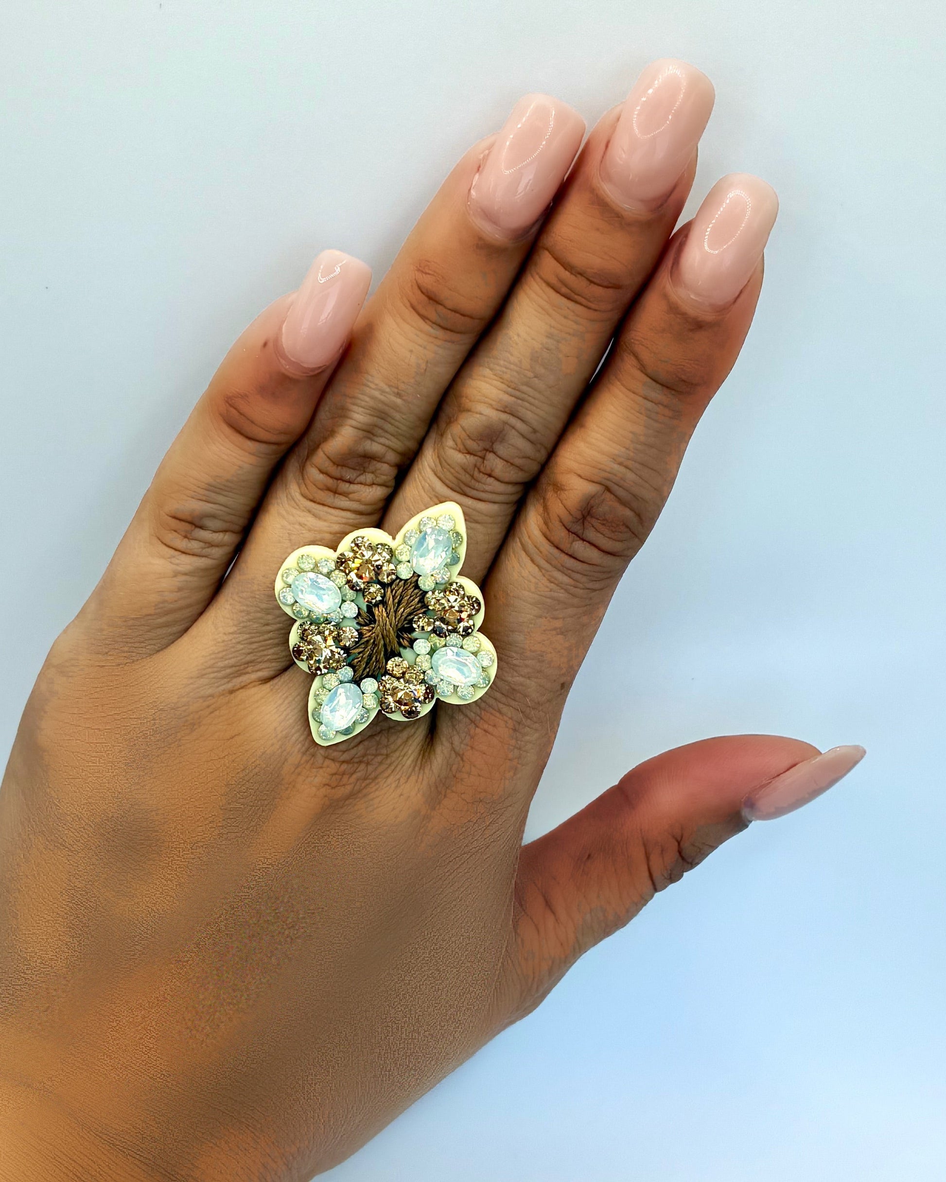 Hand wearing a decorative ring with gemstones on a light background