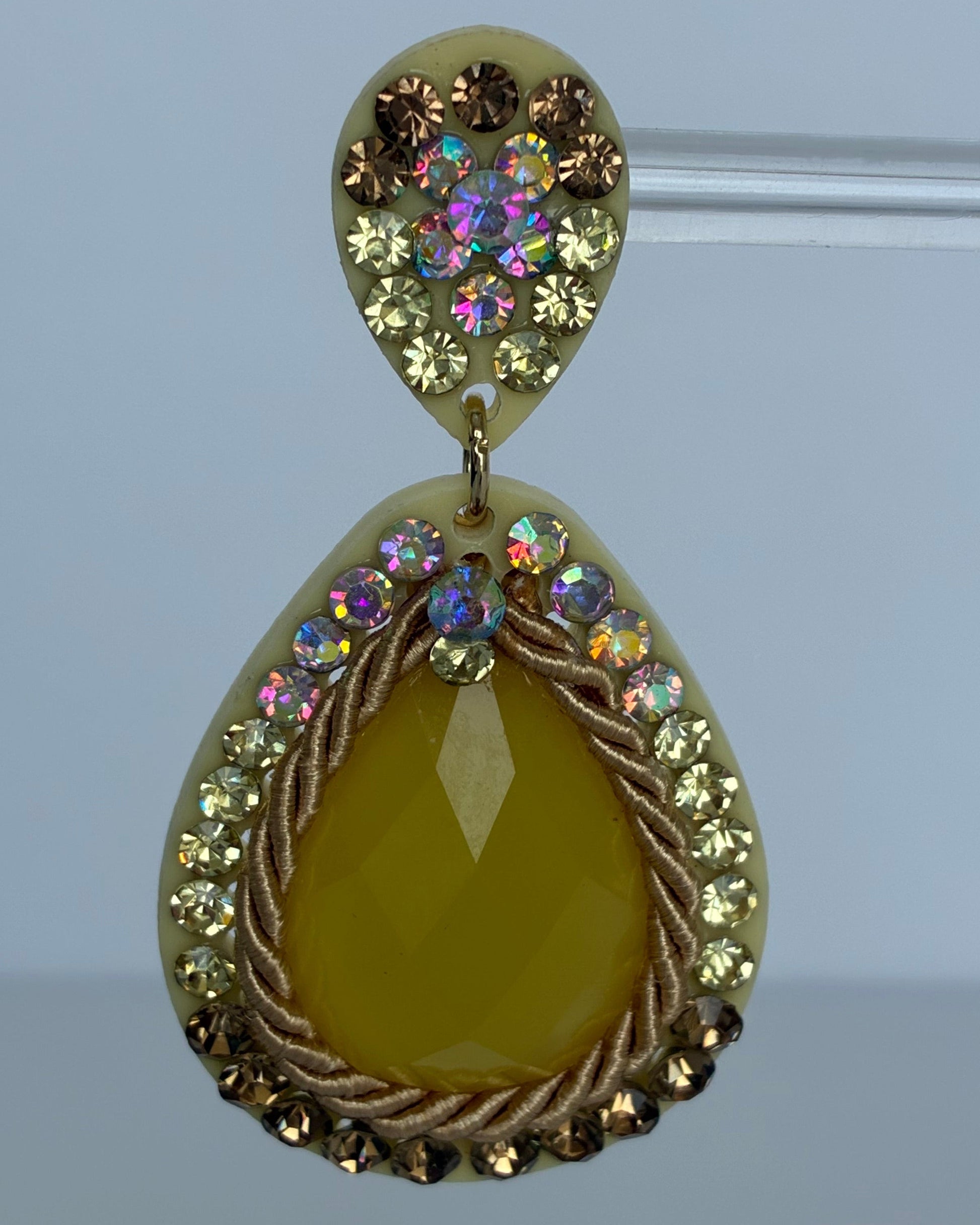 Teardrop-shaped earring with yellow center and multicolored gemstones on a light blue background
