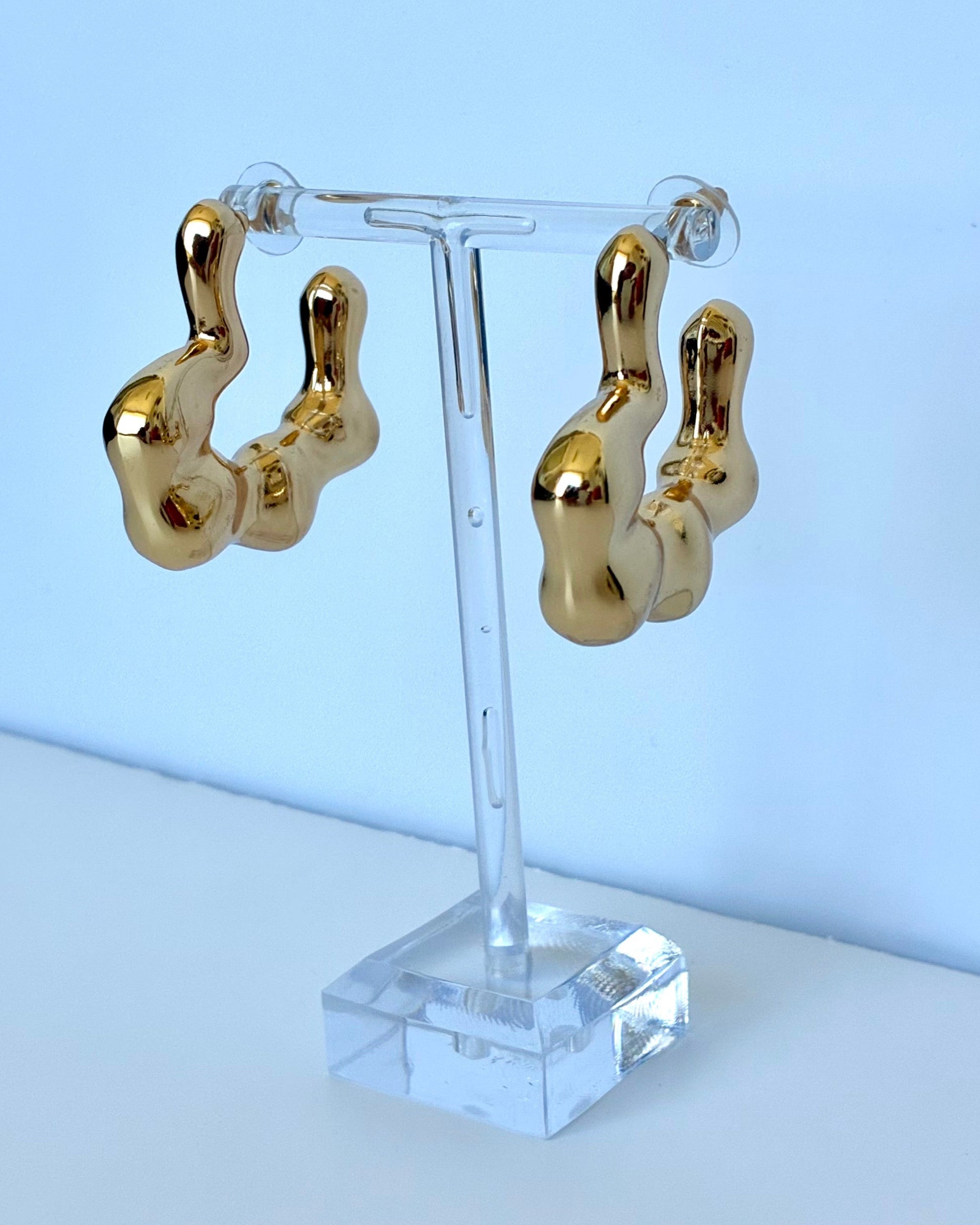 Gold hoop earrings on a clear stand against a light blue background