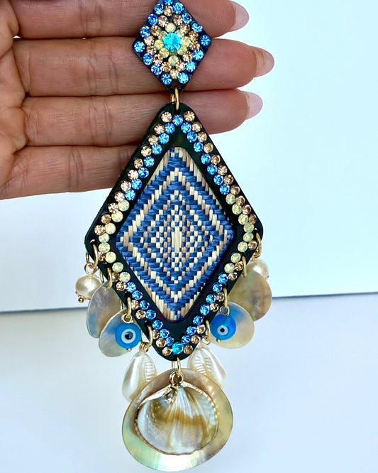 Decorative earring with blue and gold accents held by a hand against a white background