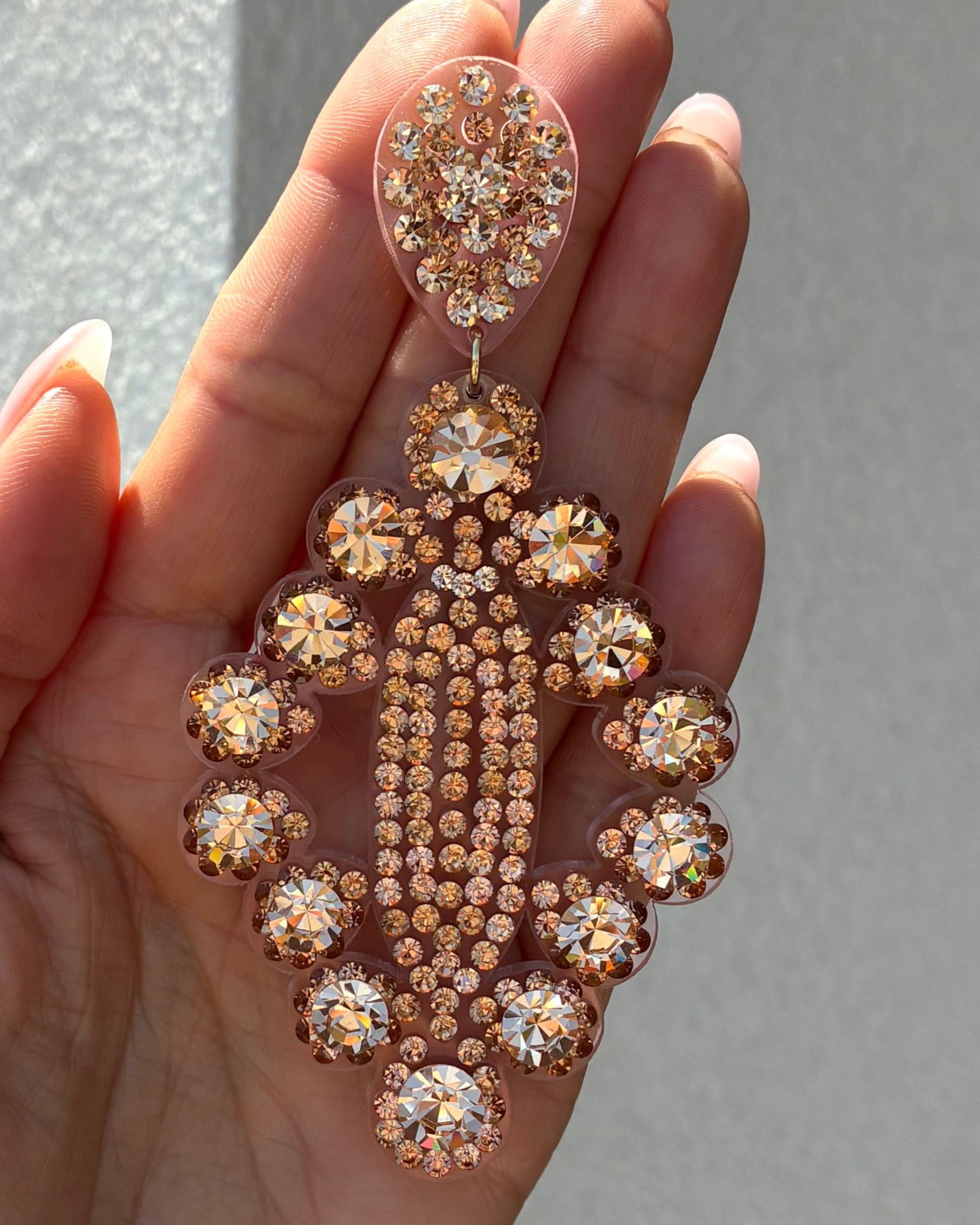 Rose gold and clear crystal earrings held in a hand against a neutral background