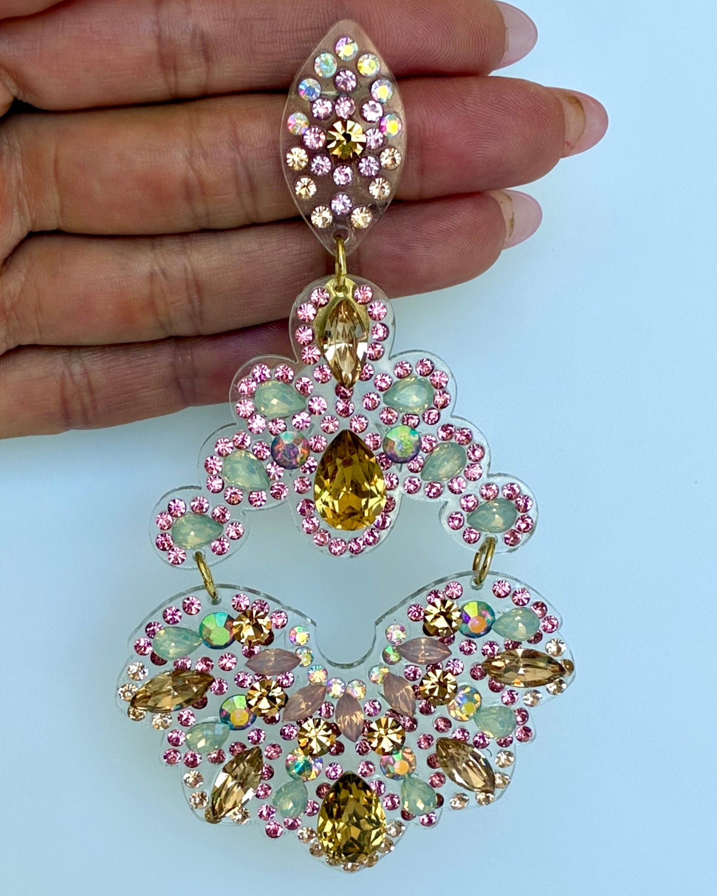 Ornate earrings with gemstones held by a hand against a light blue background