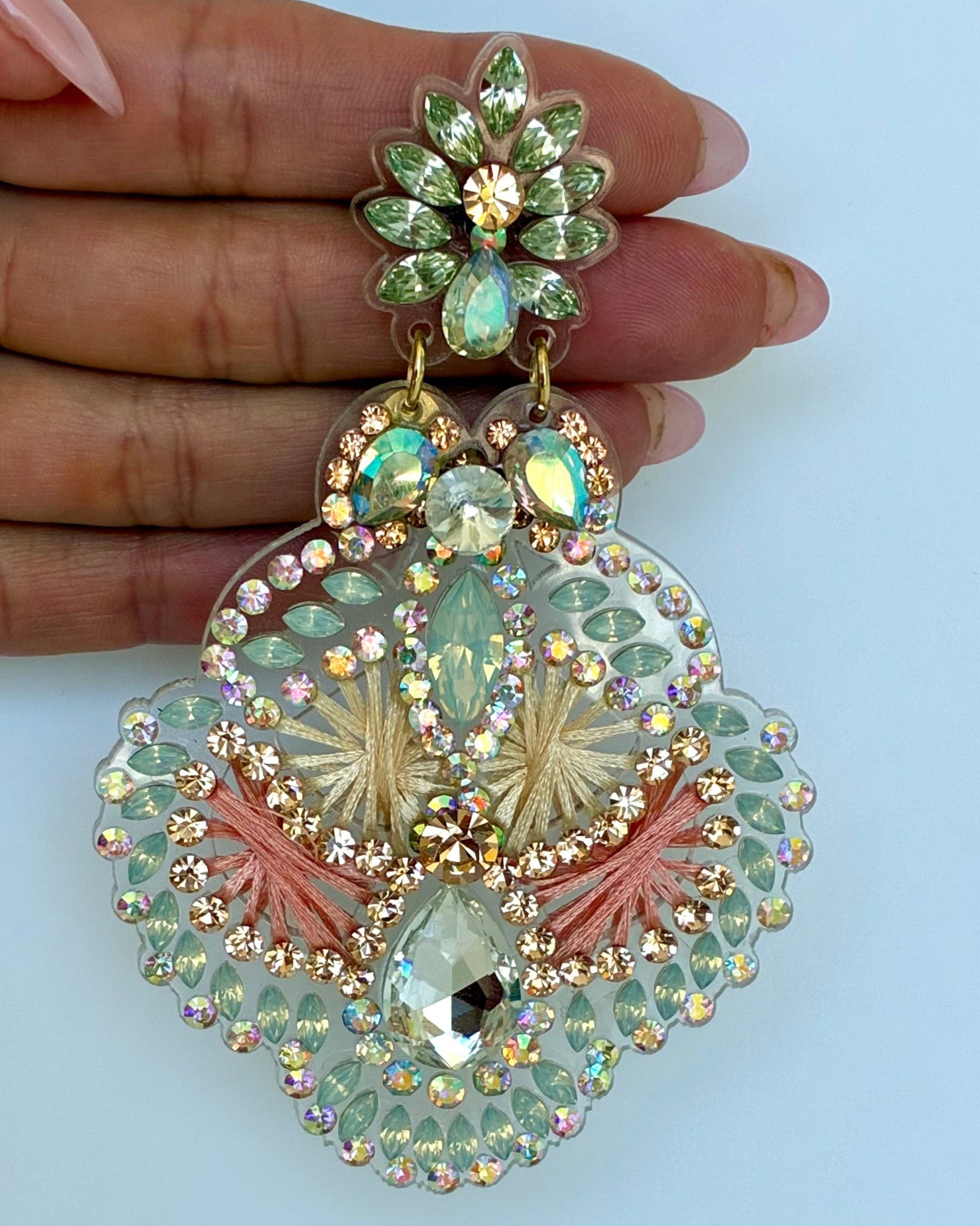 Ornate earrings with gemstones held by a hand against a light blue background