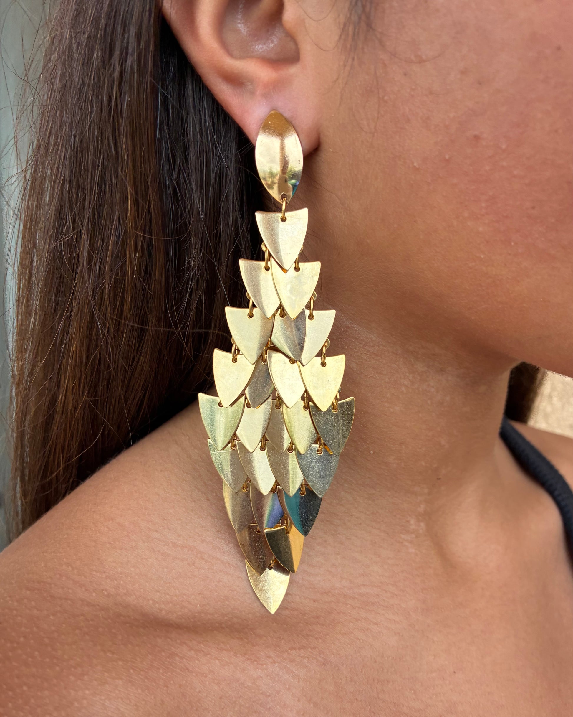 Close-up of a person wearing a gold pyramid-shaped earring.