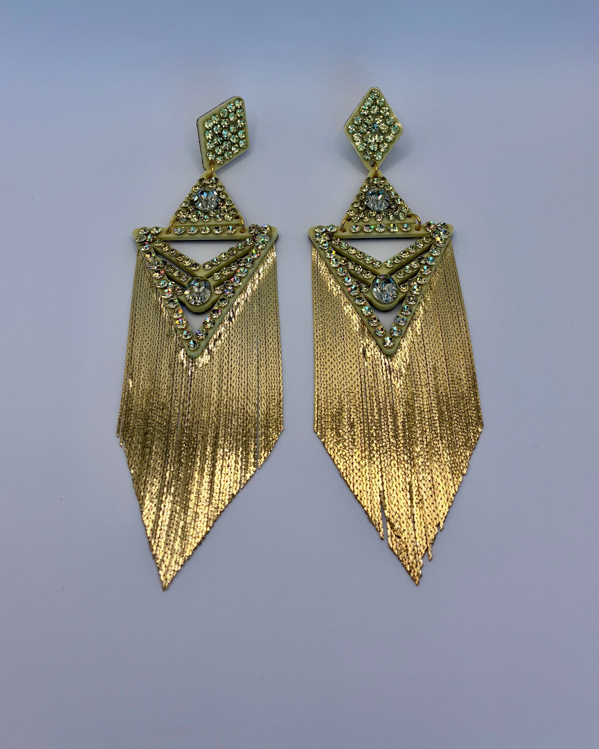 Gold fringe earrings with gemstone accents on a light purple background