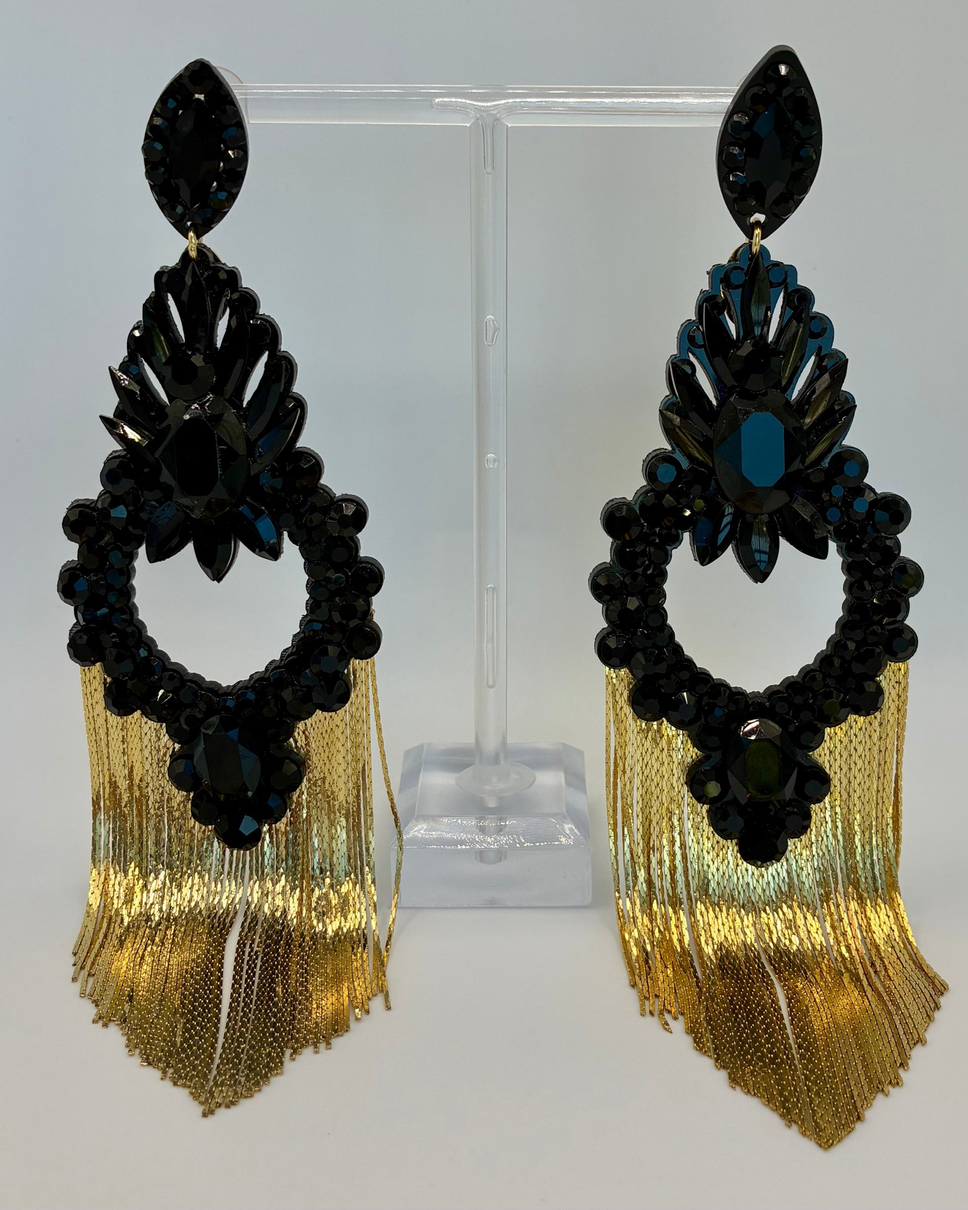Pair of black and gold fringe earrings on a clear stand against a white background