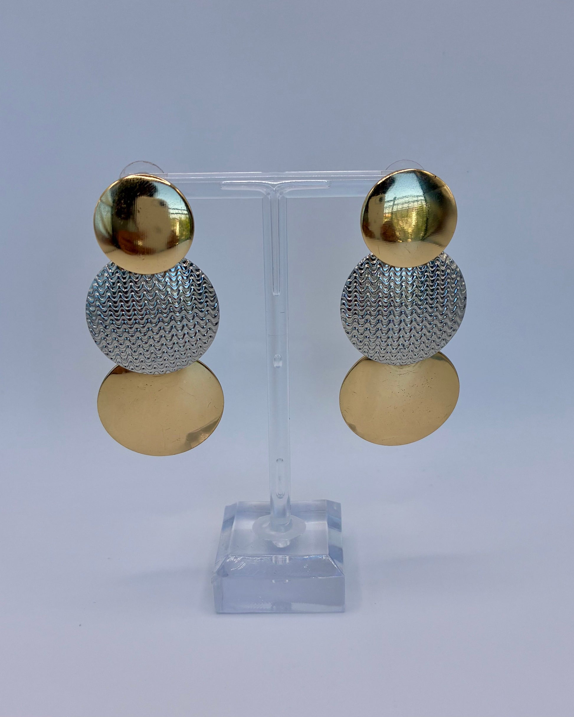 Gold and silver sphere earrings on a clear stand against a light gray background