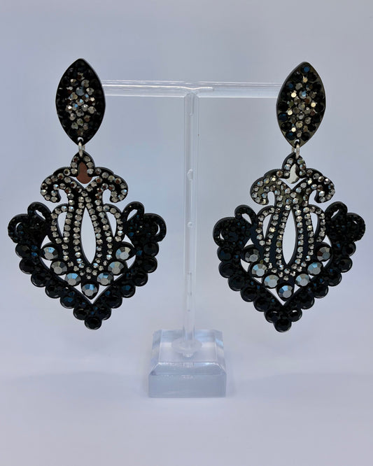 Pair of black chandelier earrings on a clear stand against a light gray background