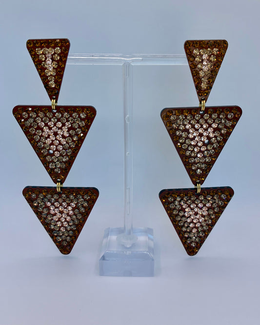 Triangular earrings with rhinestone embellishments on a clear stand against a light gray background
