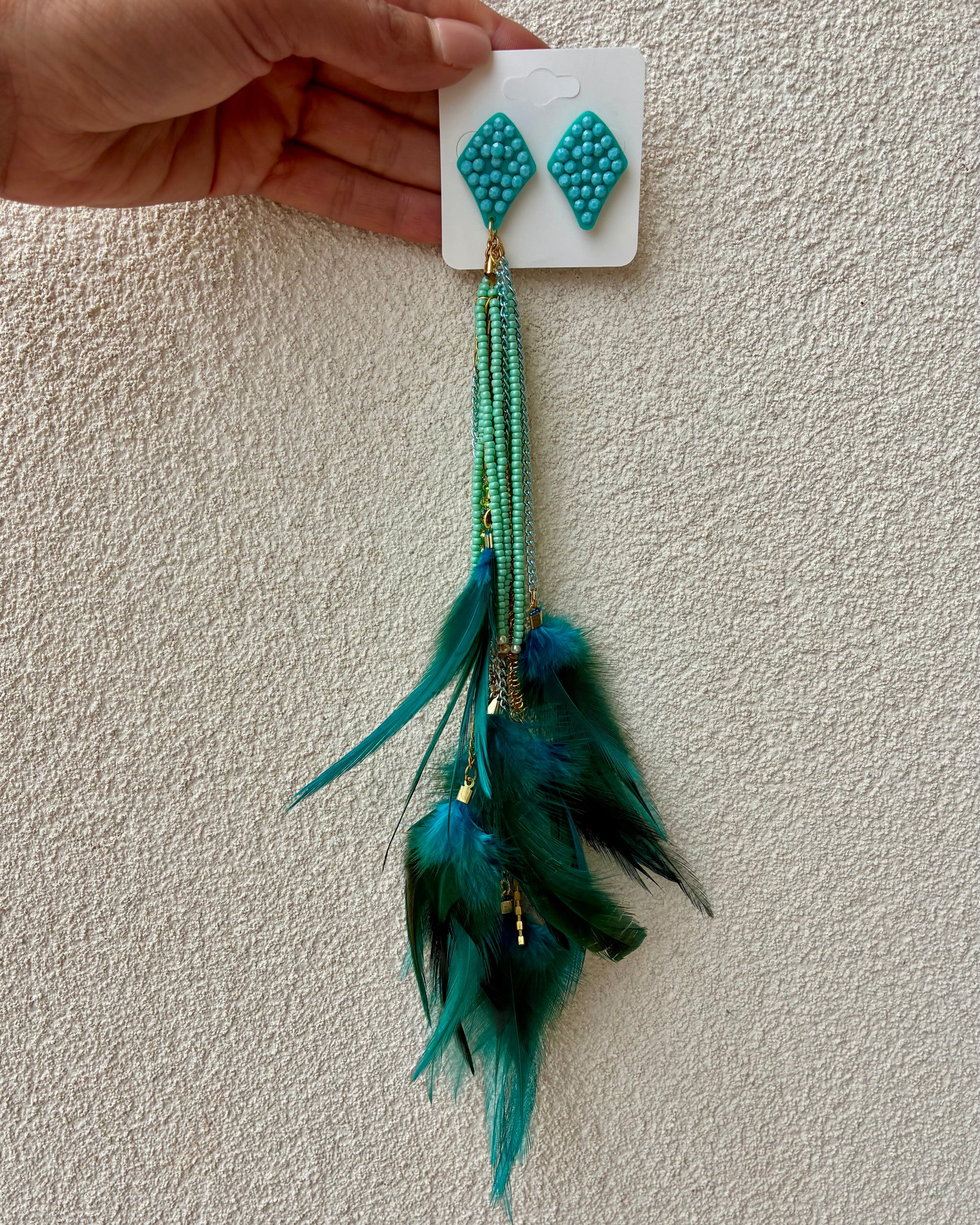 Turquoise beaded earrings with feathers on a beige background