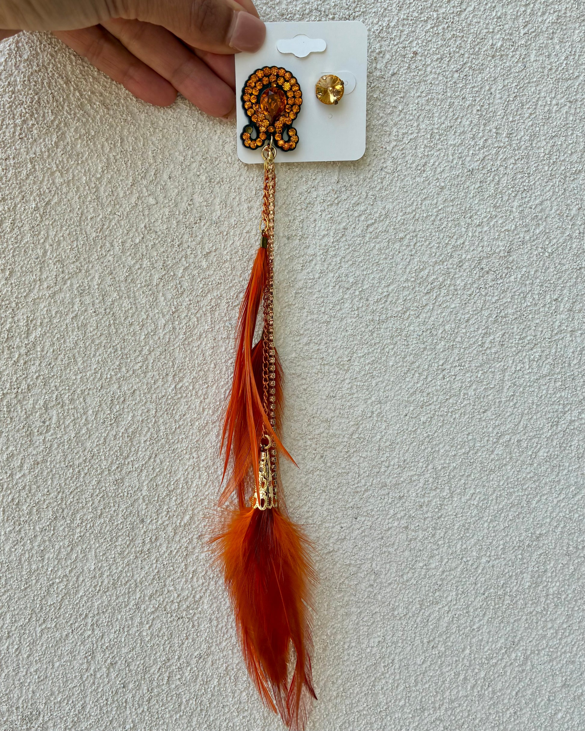 Feathered earring with orange feathers on a white card against a light gray background