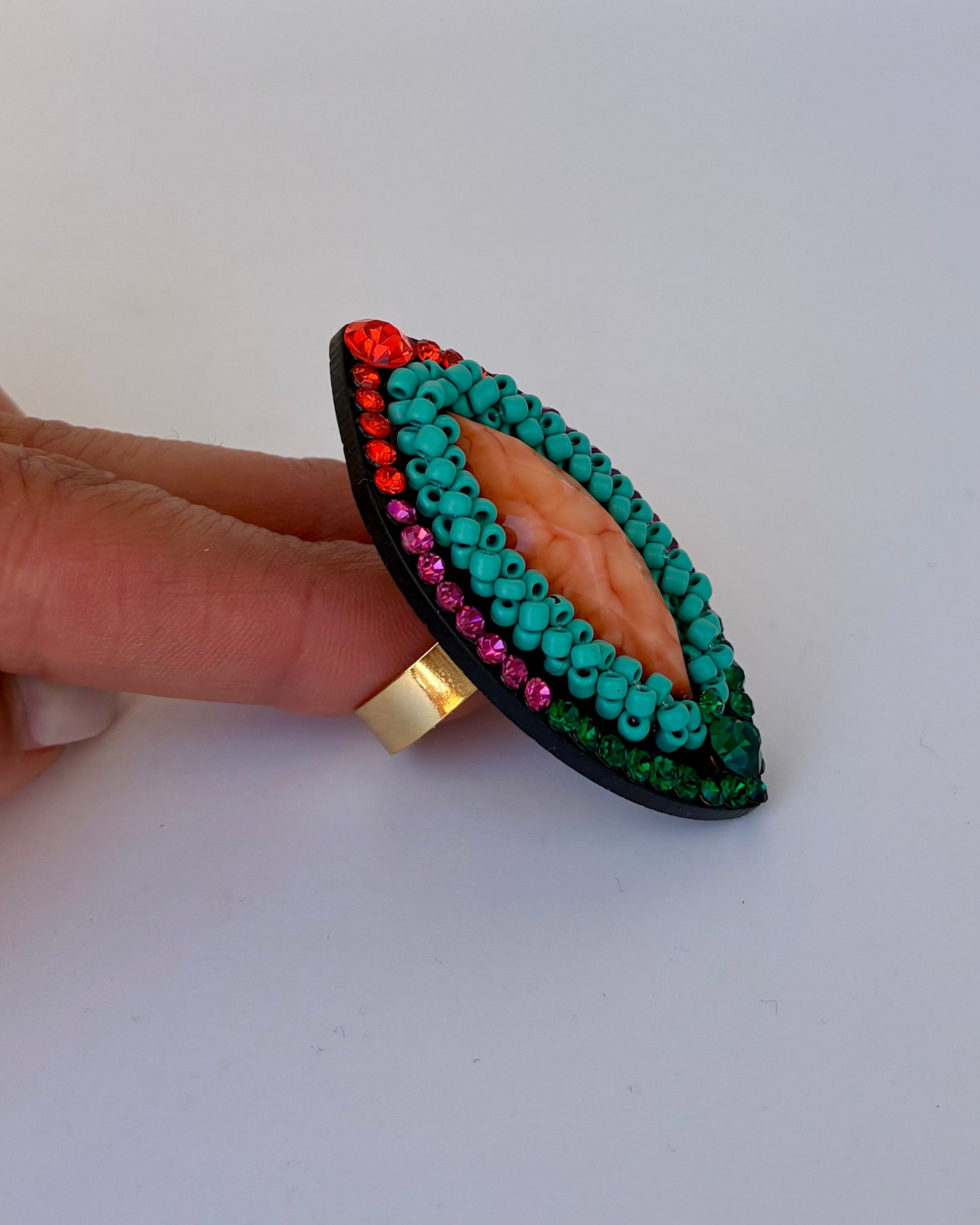 Hand holding a decorative ring with green stones and gold band on a white background