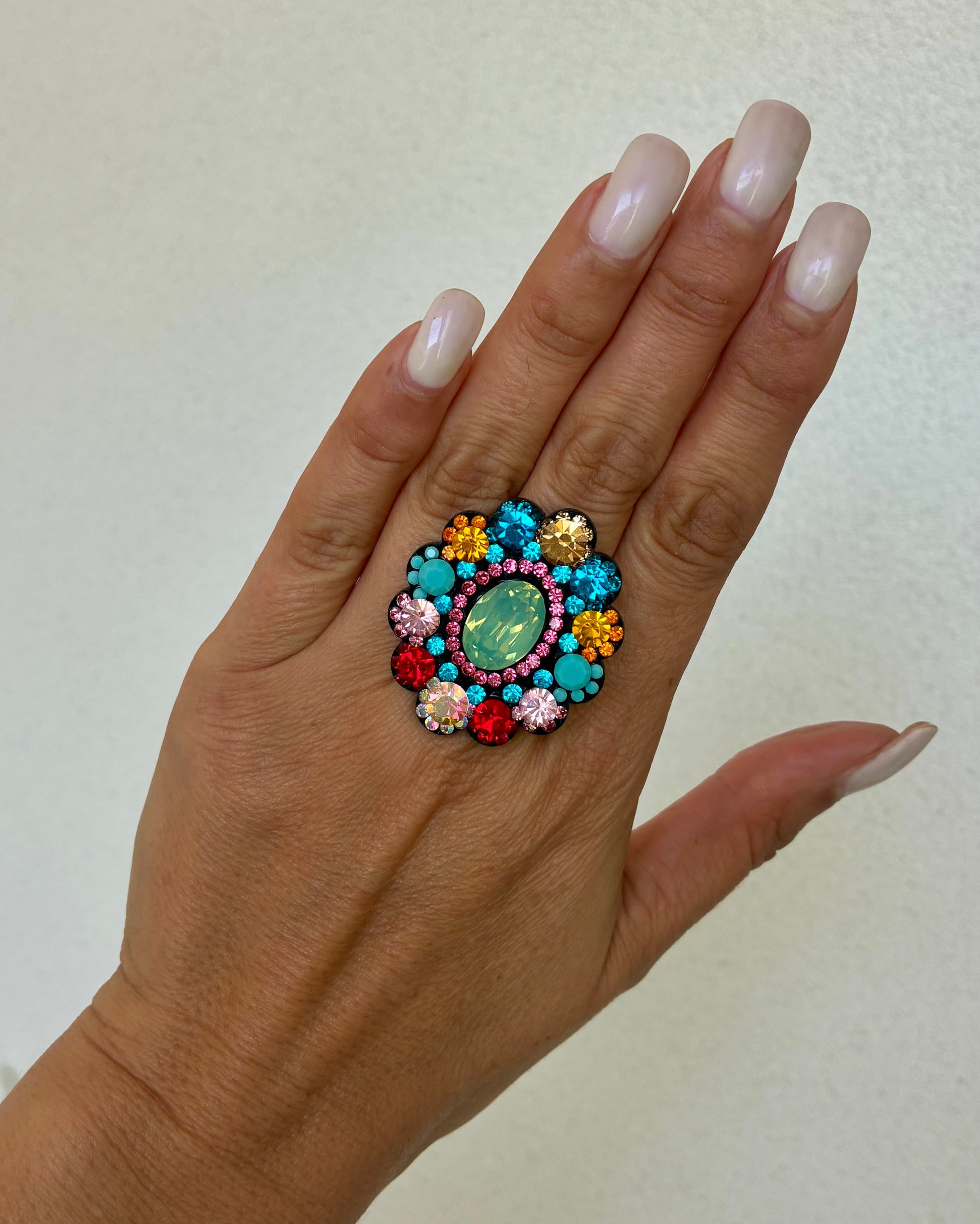 Hand wearing a colorful ring with gemstones on a plain background