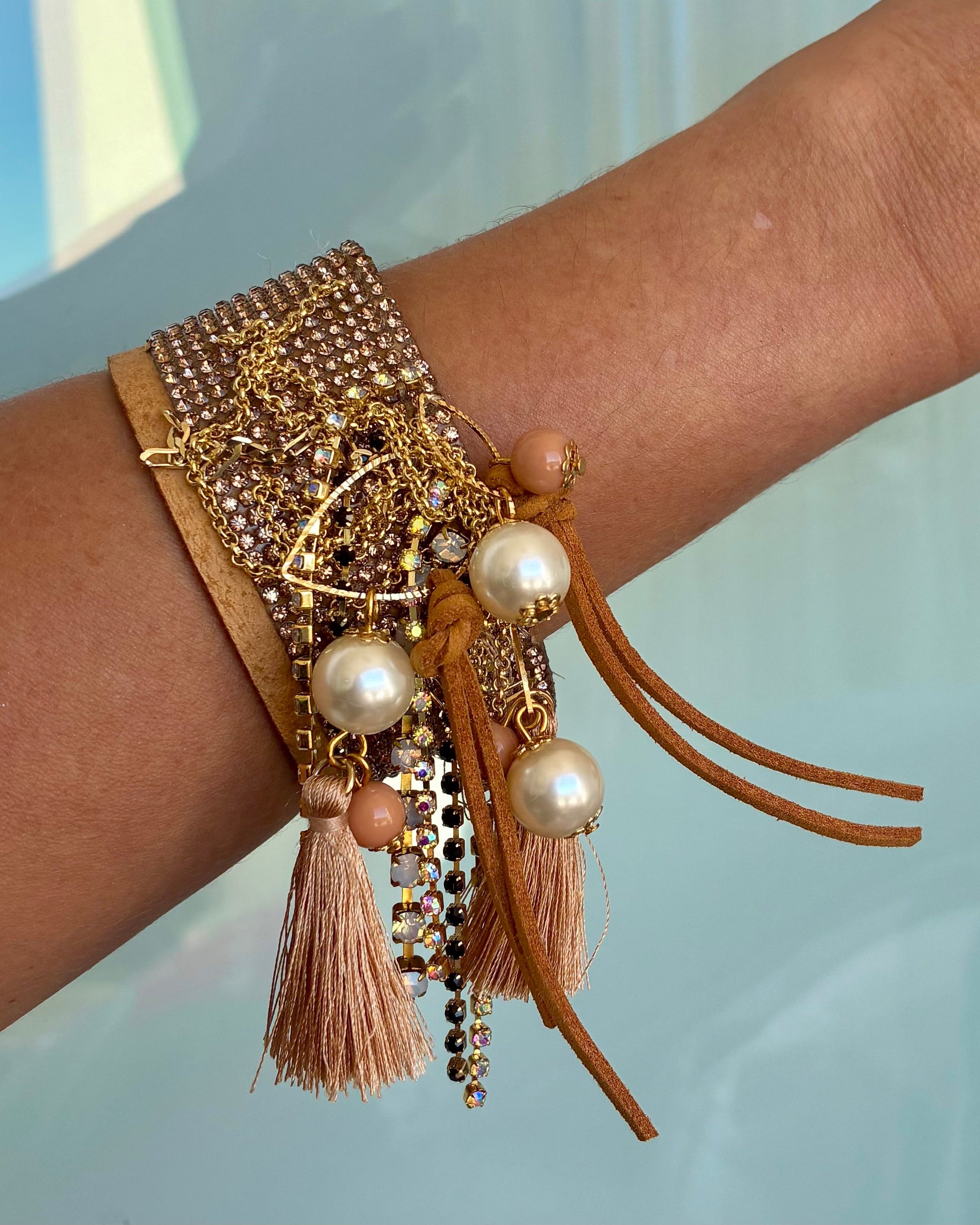 Elaborate bracelet with pearls and tassels on a wrist against a light blue background