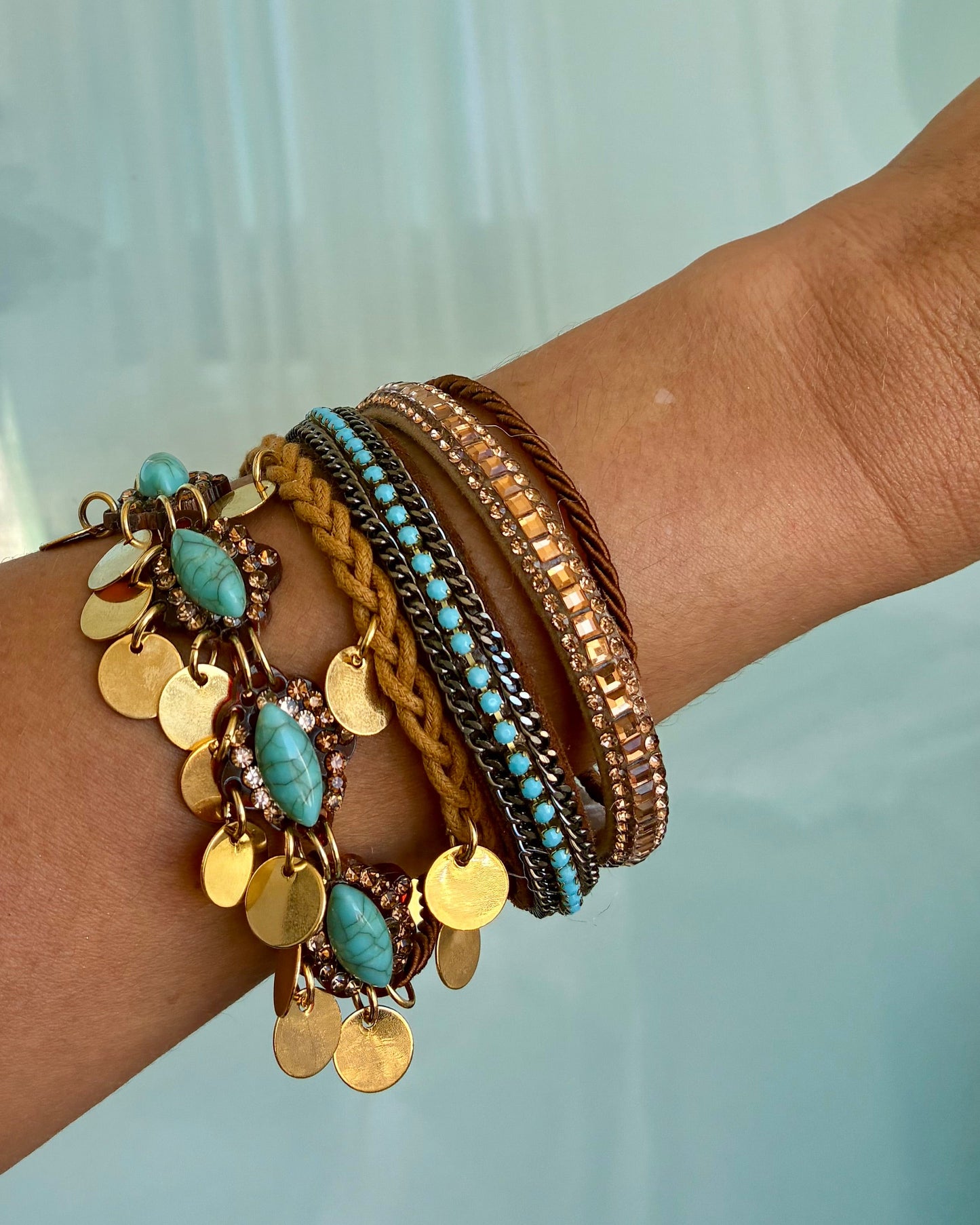 Wrist wearing multiple bracelets with turquoise stones and gold accents against a light background