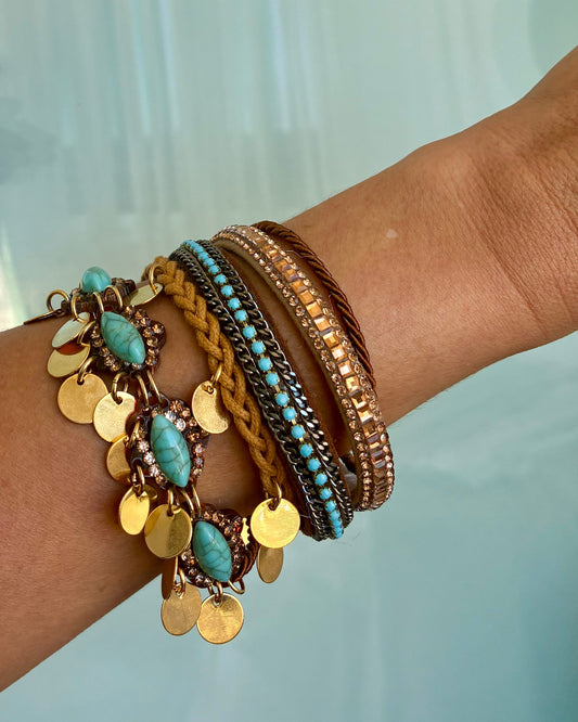 Wrist wearing multiple bracelets with turquoise stones and gold accents against a light background