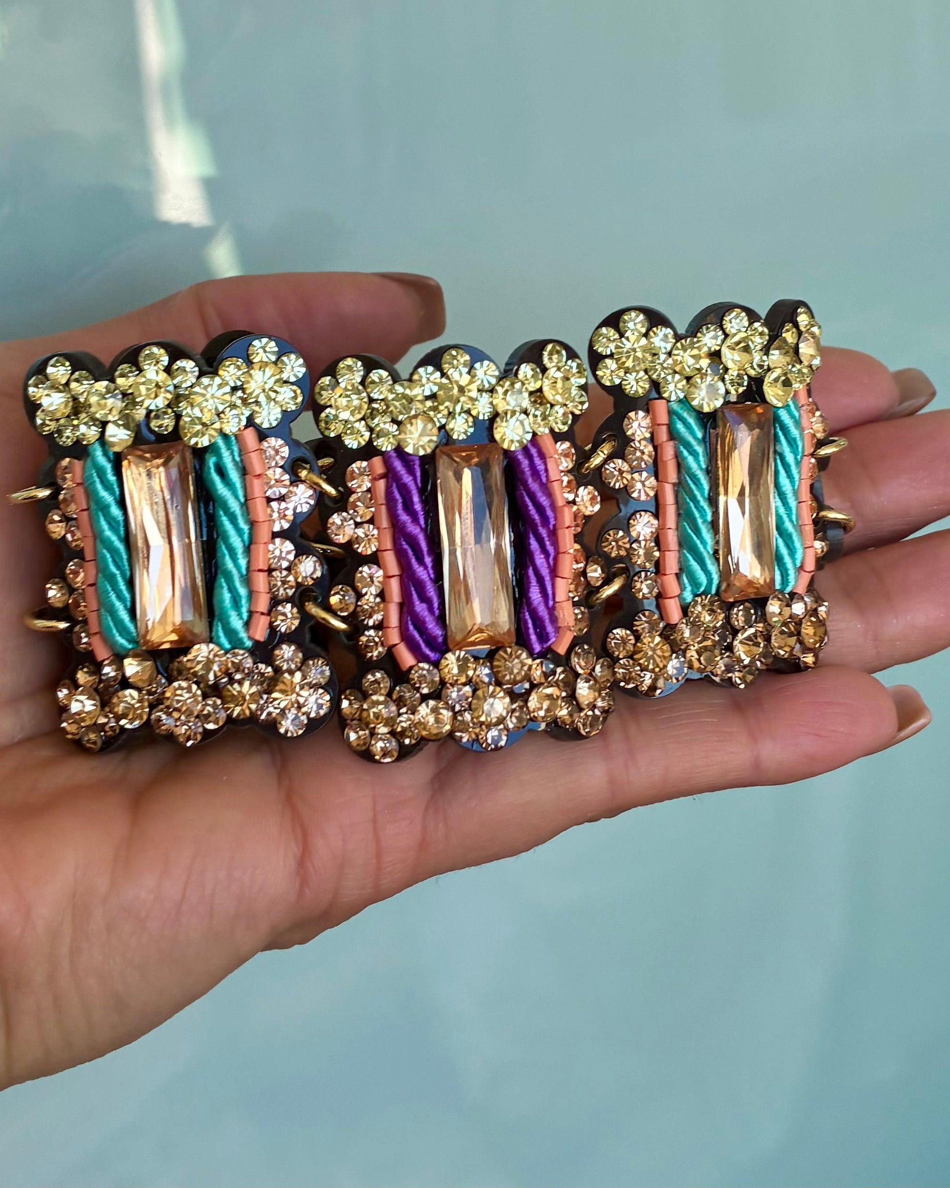 Multicolored bracelet with floral and cable designs held in a hand against a light blue background