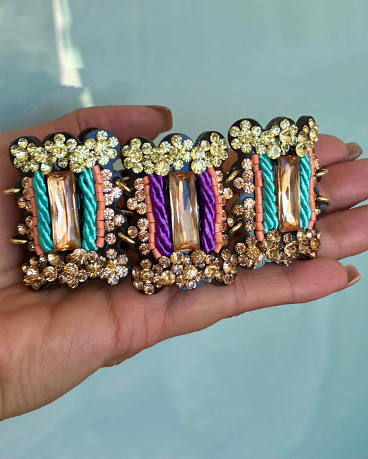 Multicolored bracelet with floral and cable designs held in a hand against a light blue background