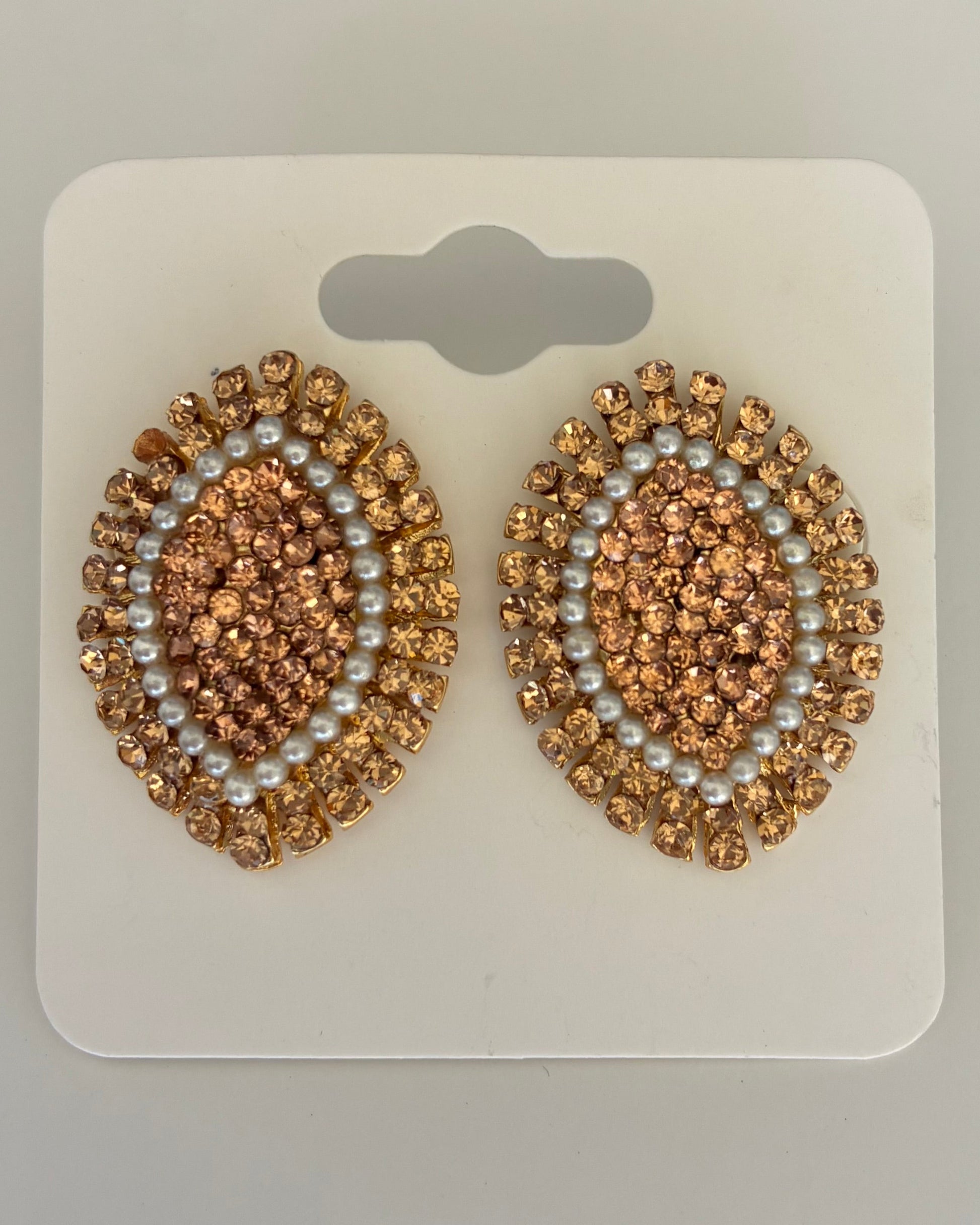 Pair of gold and pearl embellished earrings on a white card against a gray background