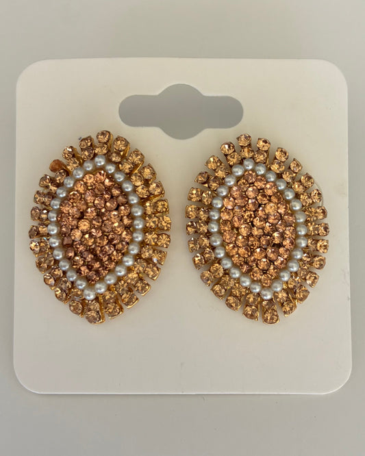 Pair of gold and pearl embellished earrings on a white card against a gray background