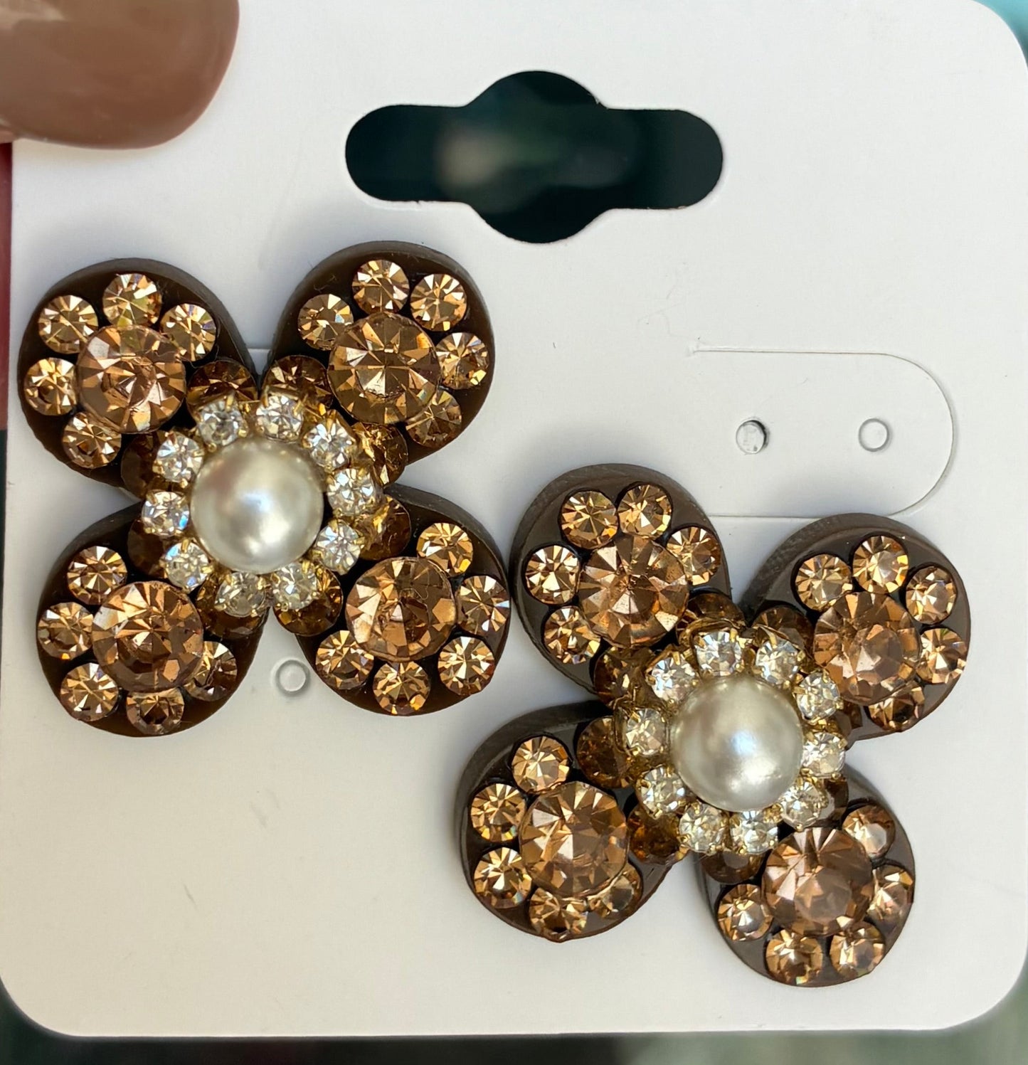 Flower-shaped earrings with gold and pearl details on a white card.